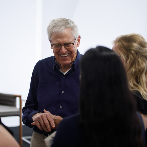 A photo of Charles Koch wearing a dark blazer and light-colored shirt smiling alongside two other people at a formal event.